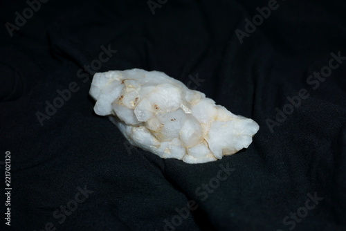 Top view of a raw milky white quartz crystal cluster on a dark fabric background. Natural geological mineral specimens for lithotherapy reiki healing and esoteric collector exhibitions design arts.