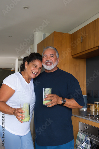 African American senior couple leaning in kitchen holding green smoothies wearing short sleeves