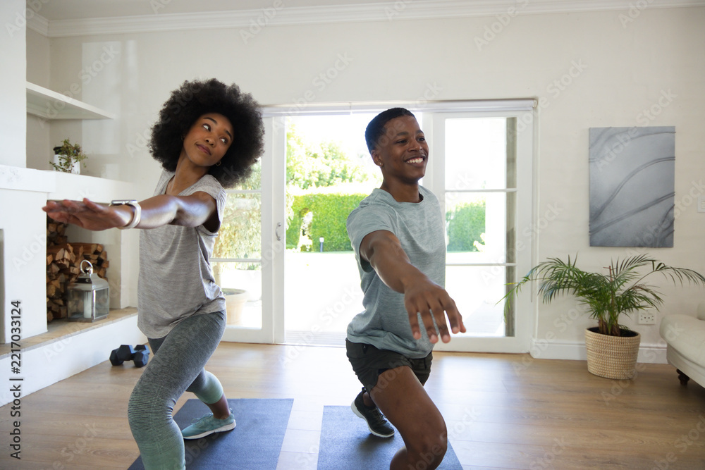Fototapeta premium African American couple doing forward lunges on dark mats in bright living room by sliding doors
