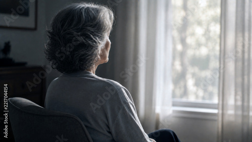 Senior woman with gray hair sitting alone by a window at home in a quiet reflective moment