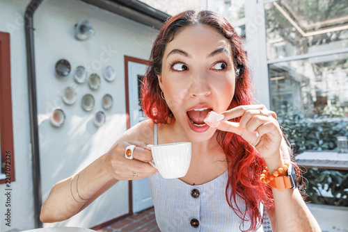 Outdoor cafe terrace setting: woman eating lokum with expressive face, holding small espresso cup. Food and lifestyle concept.