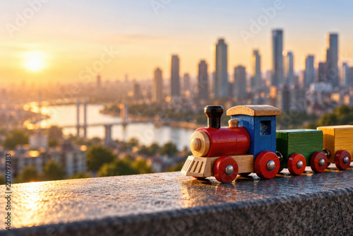Wooden toy train overlooks a city skyline at sunset. Space for text.