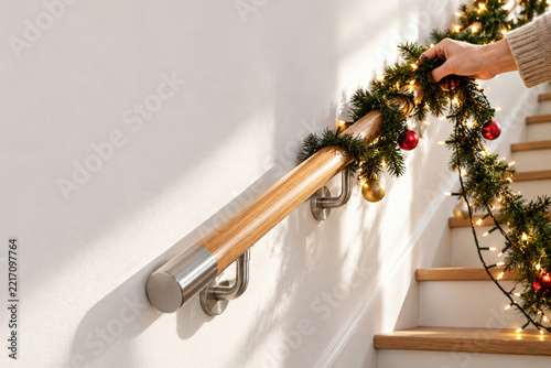 Hand decorates a staircase railing with Christmas garland. Space for text.
