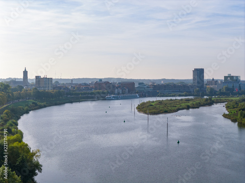 Aerial view of the Meuse river flowing through the city of Venlo with a river cruise ship, lush green riverbanks, and urban buildings, Venlo, Netherlands.