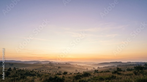 Expansive rolling hills stretching across the tranquil horizon under soft morning pastel sky tones
