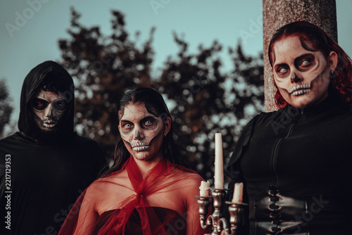 Three costumed figures with skull face paint holding pitchfork and scythe