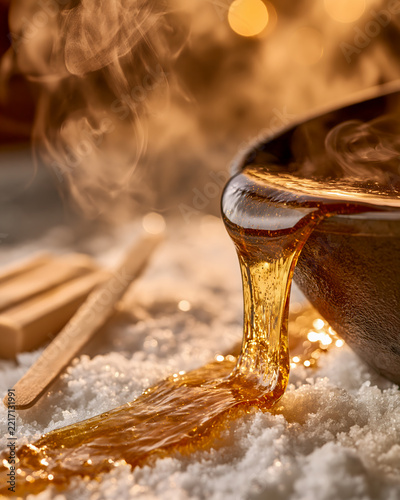 Hot maple taffy being poured in a thin stream onto clean white snow, with steam gently rising from it; a wooden stick rests nearby, ready to roll it up.