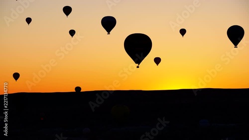 Numerous hot air balloon silhouettes floating gracefully across a vibrant orange sky during a beautiful sunrise, creating a serene and picturesque scenic view