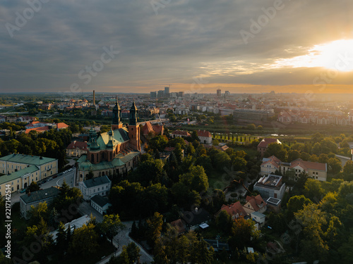 Aerial view of the Cathedral of St. Peter and St. Paul surrounded by lush greenery, historic buildings, and city skyline under a warm sunset in Poznan, Greater Poland Voivod, Poland.