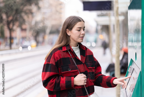 Fotografie Young woman stands with interest near the payment terminal and buys a tram ticket