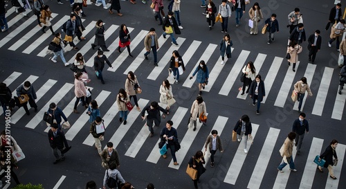 High-angle aerial shot of a bustling city intersection, large crowd of diverse pedestrians walking across wide zebra crossing lines, people in motion wearing casual autumn and winter