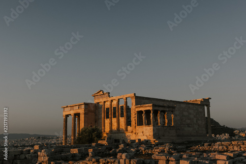 View of the ancient Erechtheion temple on the Acropolis in Athens, Greece, featuring iconic caryatid columns illuminated by warm golden hour sunlight.