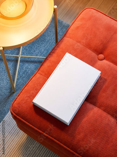 Blank white hardcover book mockup on orange corduroy sofa, top view