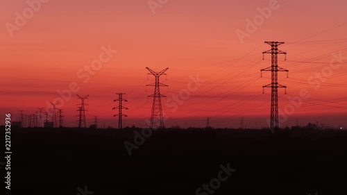 silhouette of high voltage transmission towers against a red sunset sky