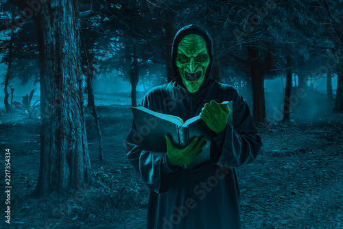 Portrait of scary witch holding magic spellbook on dark forest at night, Halloween theme