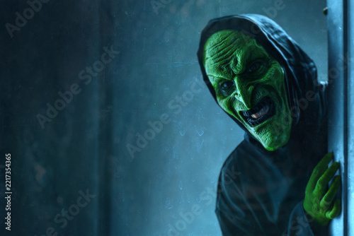 Scary witch peeking in haunted house behind wall at night, Halloween theme