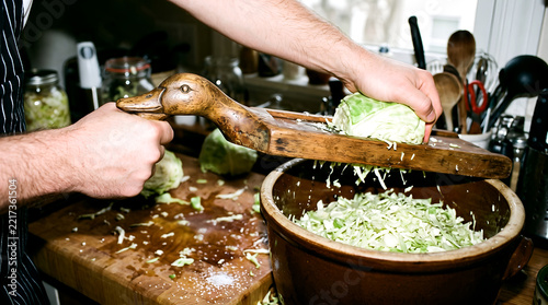 A person using a traditional wooden cabbage slicer to prepare sauerkraut in a rustic kitchen.