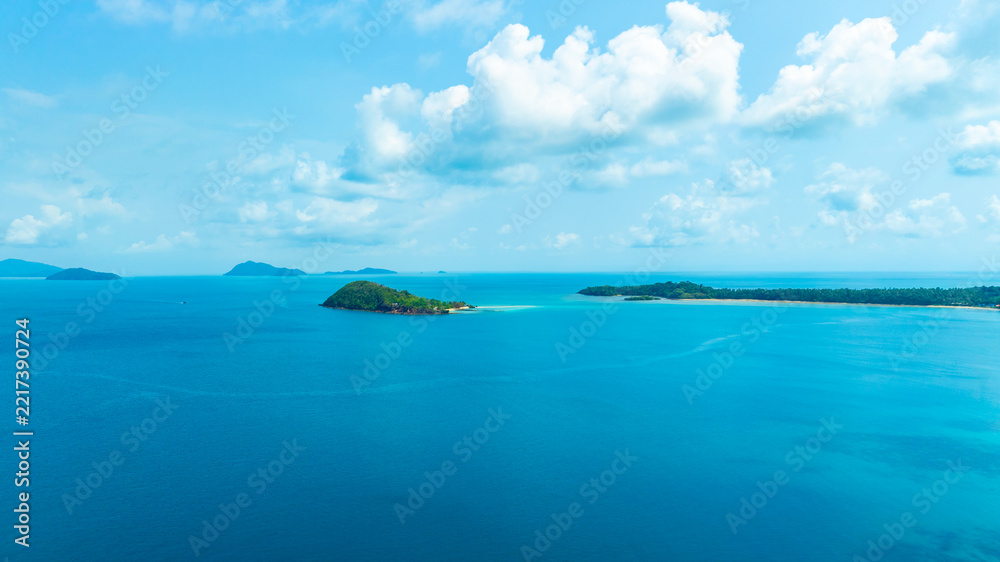 Fototapeta premium Panoramic aerial view of a lush green tropical island in the middle of a vast blue ocean under a bright sky with clouds, representing vacation, travel, and scenic nature.concept travel 
