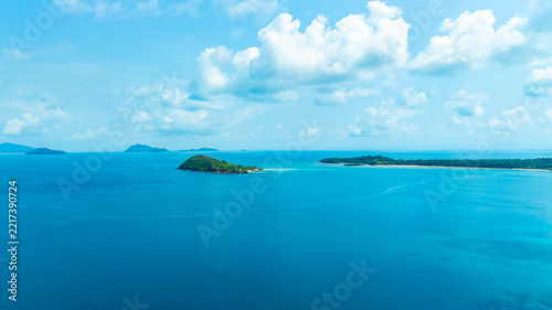 Panoramic aerial view of a lush green tropical island in the middle of a vast blue ocean under a bright sky with clouds, representing vacation, travel, and scenic nature.concept travel	