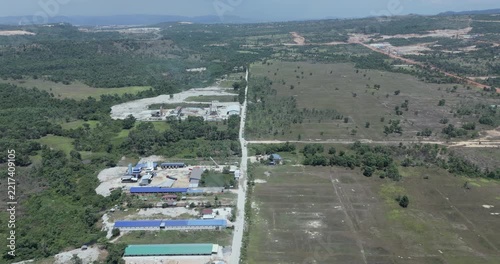 Forward aerial view displays industrial concrete plants integrated into a vast, rural landscape, featuring sprawling production facilities and storage areas divided by a long, straight road.