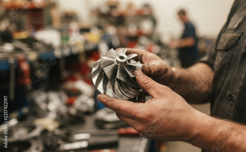 Mechanic holding a turbocharger turbine wheel in a busy auto repair shop workshop