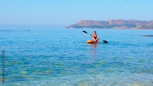 Woman paddleboard on crystal clear turquoise sea. Athletic woman in a bikini paddling her paddleboard on the calm, turquoise sea during a sunny summer day, enjoying an active vacation