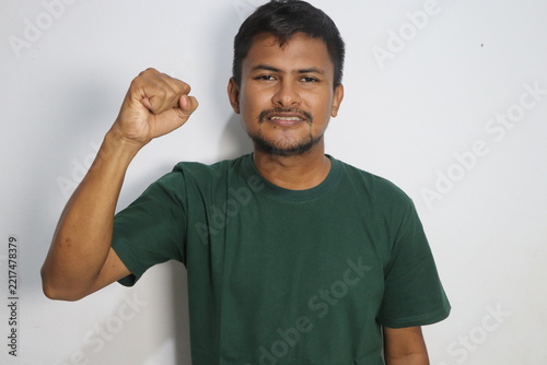 Young man raising his clenched fist with confidence wearing a green shirt