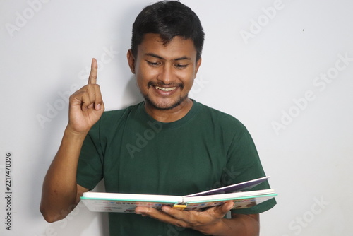 Young man reading a book and raising index finger having an idea