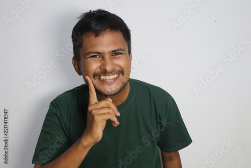 Young man smiling and pointing finger on cheek against white background