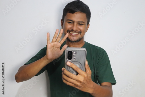 Young man smiling and waving hand during a video call on his smartphone against a plain white background