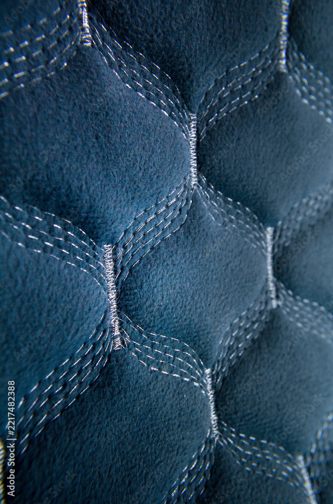Fototapeta premium A detailed macro close-up of a blue quilted textile fabric featuring an intricate geometric pattern with silver stitched lines.