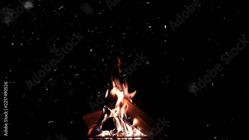 A campfire flickers as snow falls through the dark Christmas night, with space for text.