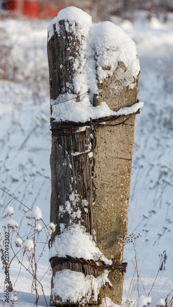 Fototapeta premium Snow blankets a weathered wooden fence post
