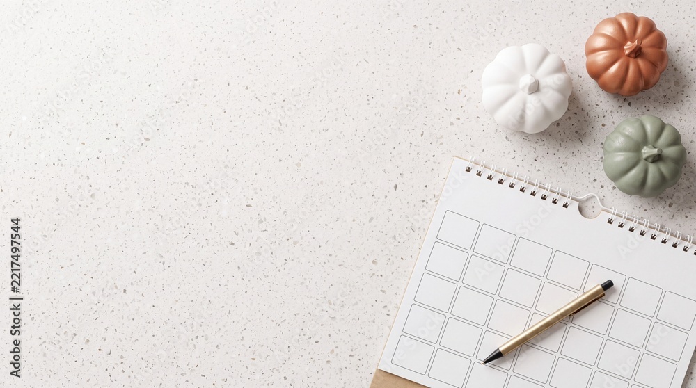 Fototapeta premium Minimalist Autumn Planning Still Life with Blank Monthly Calendar Planner, Gold Pen, and Decorative Pumpkins on White Granite Surface with Large Negative Space on Left for Text