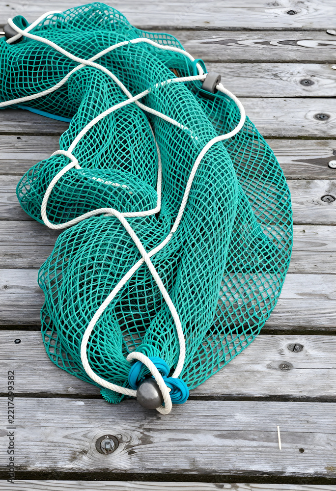 Fototapeta premium Sustainable fishing and marine conservation, green commercial fishing net with weights on a weathered wooden dock for maritime industry and ocean safety