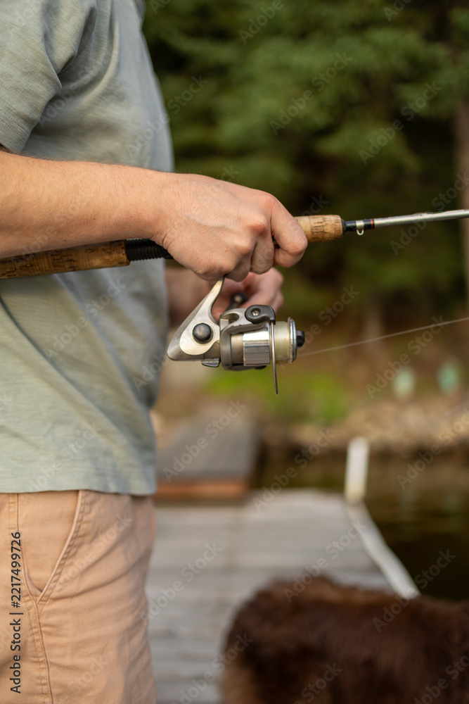 Fototapeta premium Man holds a fishing rod while standing on a dock