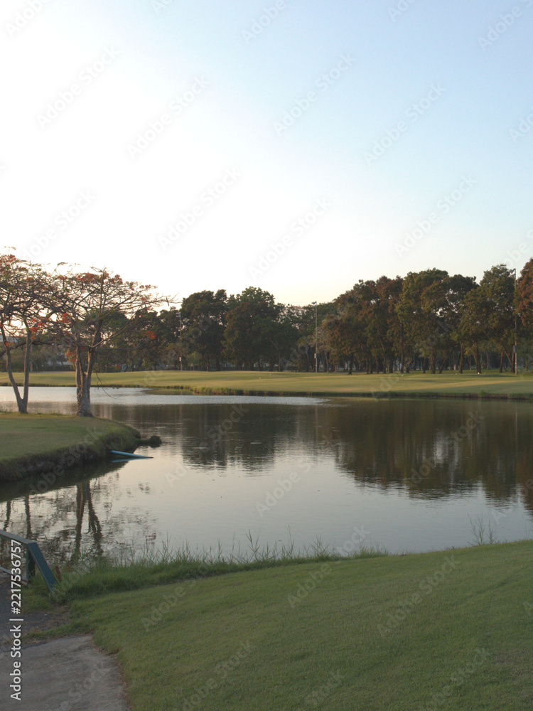 Naklejka premium Tranquil Golf Course Pond Surrounded by Trees and Green Lawns