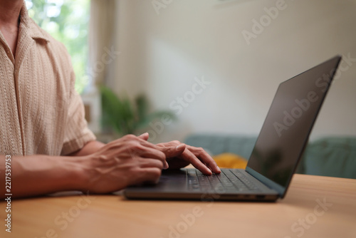 Asian man typing on a laptop at home setting, capturing remote work, digital productivity and a flexible modern workplace.