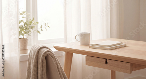 Minimalist wooden desk with white mug and notebooks by sheer curtains in home office
