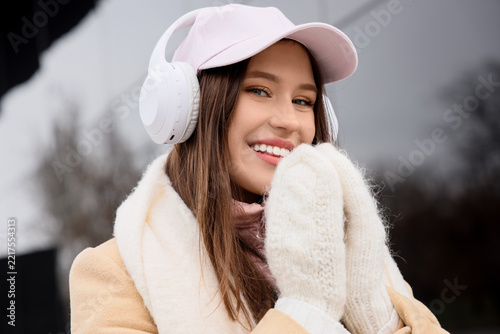 Young woman in stylish winter clothes and with headphones on city street