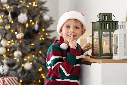 Obraz na plátně Christmas surprise and holiday magic, little boy in santa hat making a hush gest
