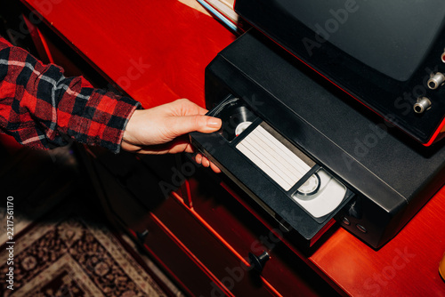 female hand inserts a VHS tape into a VCR, evoking a sense of nostalgia and memories while preparing to watch old home videos from the 90s