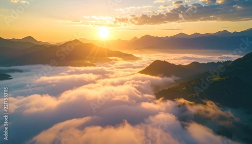 A majestic sunrise casting golden rays over a sea of clouds nestled between mountain peaks. The sky is a vibrant canvas of orange, yellow, and pink hues, promising a new day
