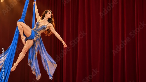 Female Aerial Silk Performer in Blue Fabric Beside Red Velvet Drapes