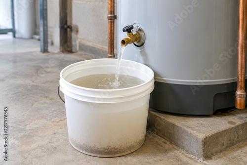 Cloudy water and sediment draining from water heater valve into white bucket - hard water tank flush service