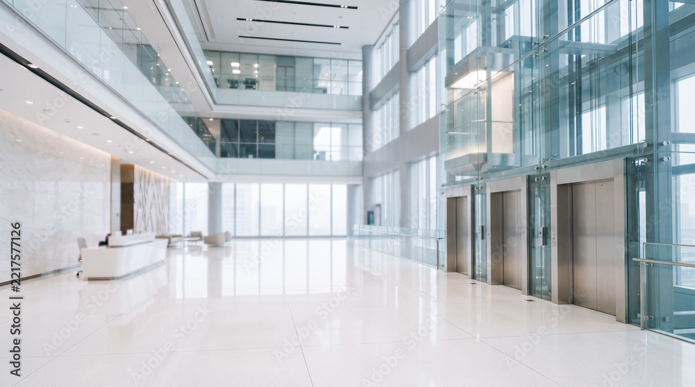 Fototapeta premium Extremely bright spacious modern corporate facility lobby featuring white marble floor beside glass elevator shafts and distant reception desk without people
