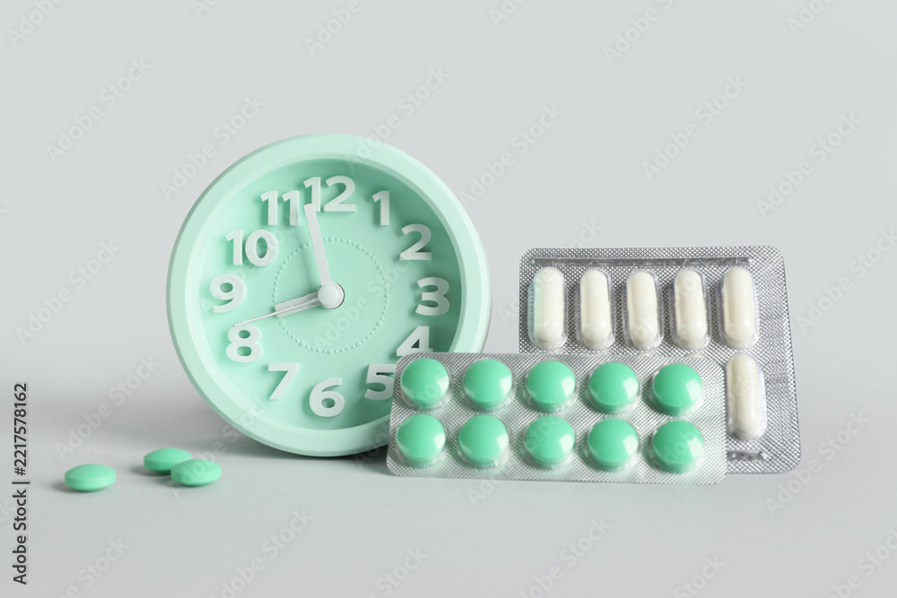 Naklejka premium Medication adherence and healthcare schedule, clock with pill blisters and tablets for daily treatment routine and medical management on grey background