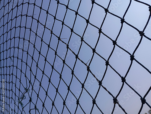 Broken black rope net against clear blue sky