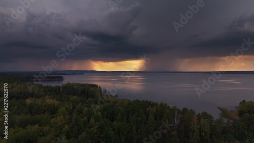 Storm with lightning over the lake. Aerial view of the coast of the lake with the stormy clouds forming in the sky, rain falling on the horizon and lightning flashing. The Kama river, Russia