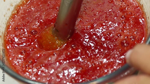 Immersion blender pureeing fresh red strawberries in a glass bowl. High angle close up shot.